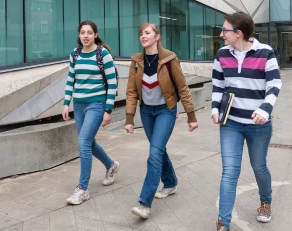 Three postgraduate students walking past an Oxford science building